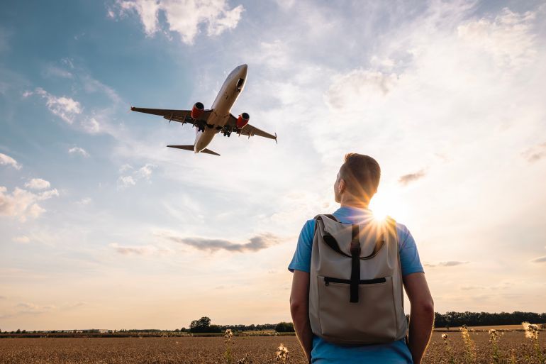 Man with backpack looking up to airplane landing at airport during golden sunset.