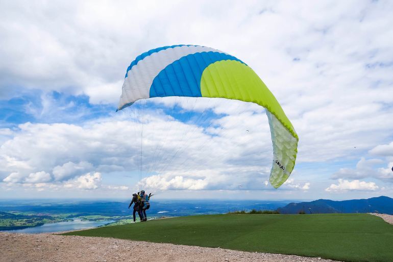Fussen, Germany - 25 July 2020: A tandem paraglider is taking off from the launch pad on top of Mt Tegelberg (elev. 1881m) in the Ammergau Alps. Since the 1970s, Mt Tegelberg is a popular take-off point for hang gliders and paragliders.