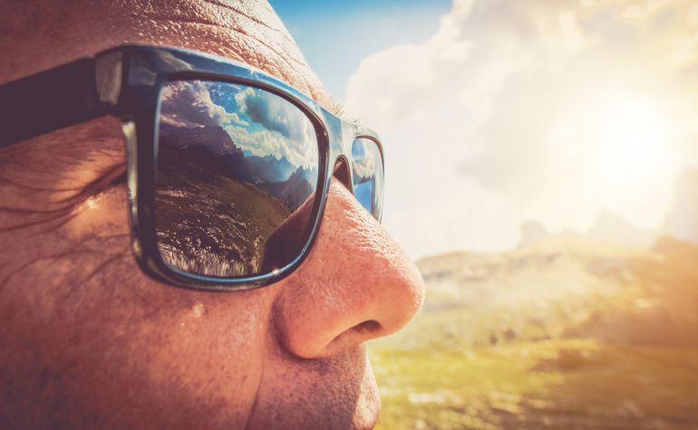أعراض سرطان العين Sunglasses Protection. Caucasian Men in His 50s in the Trendy Black Sunglasses. Closeup Photo. Mountains Reflection in the Lenses.