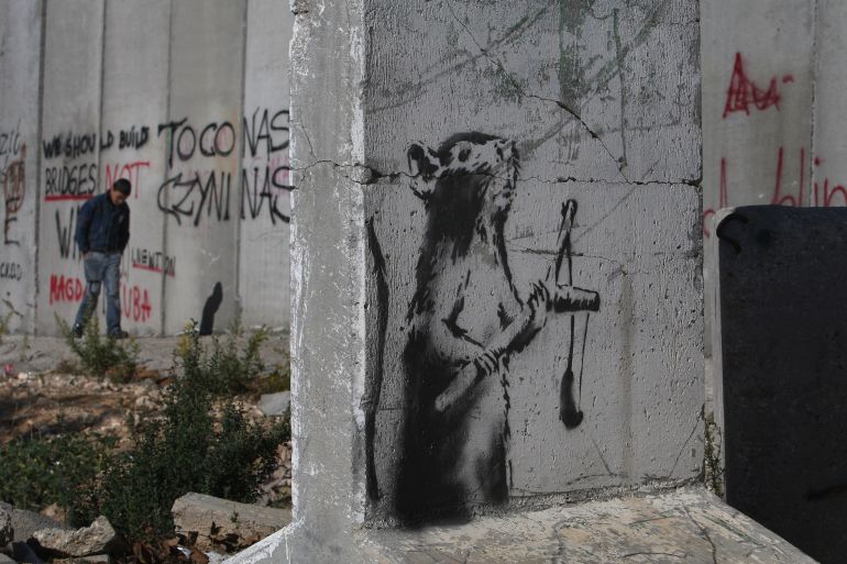 BETHLEHEM, WEST BANK - DECEMBER 05: A new stencil painting on a concrete barricade by elusive British graffiti artist Banksy shows a rat holding a slingshot December 5, 2007 opposite an Israeli army guard post (unseen) where Israel's separation barrier cuts into the biblical city of Bethlehem in the West Bank. The Bristol-born artist has adorned Israel's West Bank separation barrier and Bethlehem walls with new images, including one of a dove wearing a flak jacket and a soldier being frisked by a young girl. His works, along with those of other international artists, are part of an exhibition called Santa's Ghetto. (Photo by David Silverman/Getty Images)