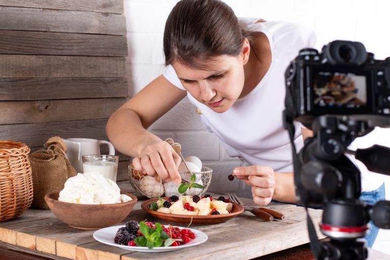 Professional food blogger taking pictures of pastry on table with dslr camera. Female photographer taking pictures of sweet food, camera mounted on tripod