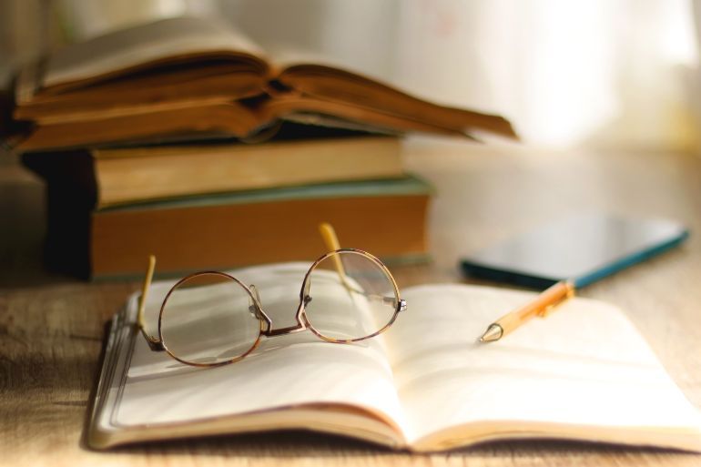 Open book, mechanical pencil, reading glasses, mobile phone and strack of books on the desk. Studying concept. Selective focus.